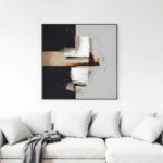 Abstract black and white geometric painting above white sofa with gray throw blanket.