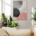 Minimalist abstract circles artwork hanging between lush plants in modern living space.