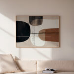 Minimalist abstract art with organic terracotta shapes in wooden frame above neutral sofa.