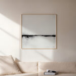 Minimalist black line abstract art on white canvas above cream sofa in sunlit room.