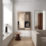 Abstract geometric artwork in minimalist white room with wooden stool and natural light.