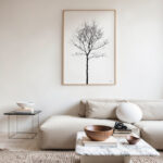 Minimalist black tree artwork above cream sofa in neutral, contemporary living room.