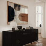 Modern abstract artwork with geometric shapes displayed above sleek black credenza in minimalist living room.