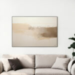 Abstract beige horizon painting above neutral sofa in minimalist living room with plant.