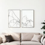 Two framed black line art prints displayed above a beige sofa with cushions.