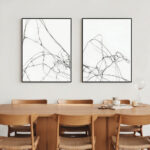 Two abstract line art drawings above wooden dining table with modern chairs