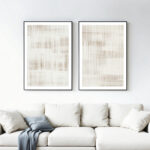 Two framed abstract line artworks in neutral tones above white sofa