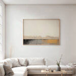Abstract artwork with warm beige tones above white sectional sofa in minimalist living room.