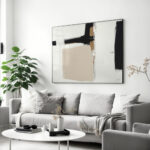 Large abstract black and beige painting over gray sofa with white coffee table.