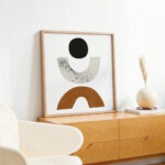 Abstract geometric art print with earth tones in wooden frame on minimalist sideboard.