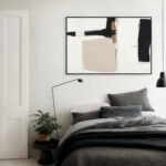 Modern abstract black and beige artwork above bed in minimalist gray bedroom.
