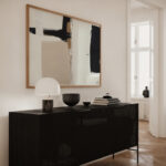 Modern black sideboard with abstract art on white wall above herringbone wood flooring.