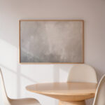 Minimalist room with wooden table, white chair and framed abstract gray artwork.