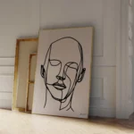 Black continuous line portrait art leaning against white wall in minimal setting.