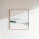 Framed abstract landscape painting with muted green and blue tones on white wall.