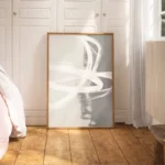 Abstract white brushstrokes on gray canvas leaning against wall in minimalist bedroom.