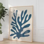 Minimalist blue coral artwork in wooden frame leaning against white wall.