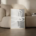 Minimalist white abstract artwork leaning against beige sofa in modern living room.