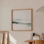 Minimalist abstract landscape painting in wooden frame above curated book display.