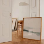 Minimalist interior with abstract blue-green artwork and natural wood furnishings.