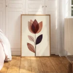 Large framed abstract flower art print with reddish-brown and purple translucent shapes, leaning on a light wooden floor in a minimalist bedroom with warm, soft lighting and neutral bedding.
