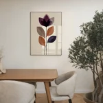 Framed abstract flower art print with layered purple and brown shapes, displayed on a neutral wall in a contemporary dining room with a wooden table, chairs, and a large potted olive tree.