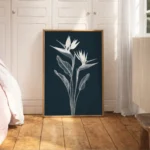 Large framed white line art of Bird of Paradise flowers on a dark navy background, leaning on a light wooden floor against white built-in wardrobes in a modern bedroom with pink bedding.
