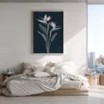 Framed white line art print of Bird of Paradise flowers on a dark navy background, hung above a low bed with neutral bedding in a minimalist bedroom with a city view from the window.