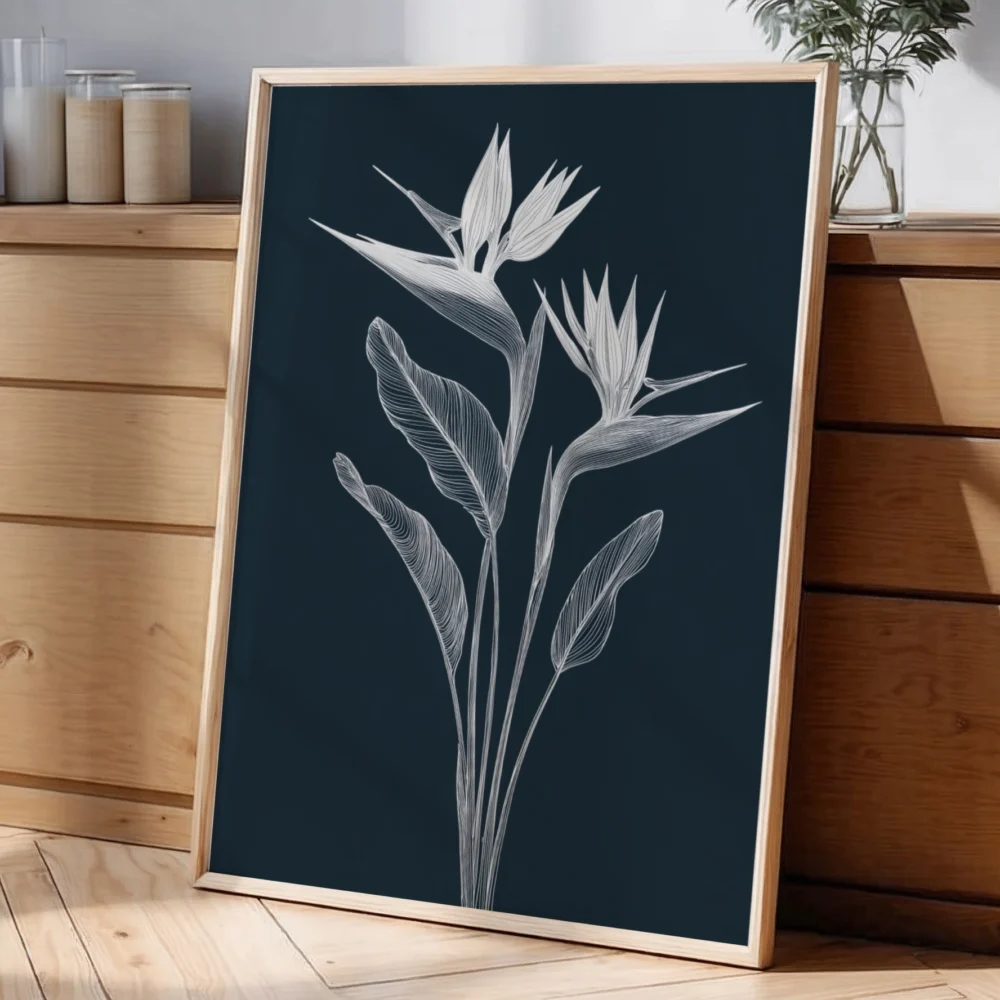Framed white line art print of Bird of Paradise flowers on a dark background, leaning against a light wall on a wooden dresser with a glass vase and decorative items.
