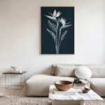 Framed white line art print of Bird of Paradise flowers on a dark navy background, hung above a light grey modular sofa with a marble coffee table in a modern living room.