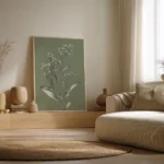 Large framed botanical illustration of a white-flowered plant on an olive green background, leaning on the floor against a light wall in a neutral-toned living room.