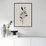 Black framed black and white botanical branch art print, displayed above a sleek white console table with minimalist decor in a modern living space.