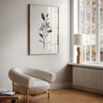 Framed black and white botanical branch art print, displayed on a wall next to a large window and a light-colored armchair, creating a serene reading nook.