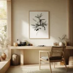 Framed black and white line art print of a leafy branch, displayed on a light wall above a wooden desk and chair in a bright, minimalist home office setting.