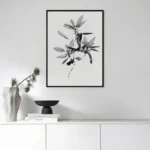 Black framed black and white line art print of a leafy branch, displayed above a sleek white console table with minimalist decor in a modern living room.