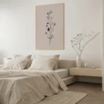 Framed black and white botanical sprig art print on a blush background, hung above a modern bedside table next to a bed with neutral-colored bedding in a bright bedroom.