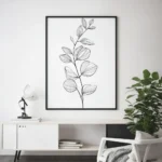 Black framed black and white botanical sprig line art print, hung on a white wall above a modern white console table with decor and a large potted plant.