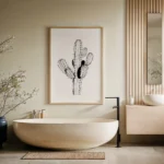 Framed black and white line art print of a cactus, hung on a light wall in a serene, spa-like bathroom with a freestanding beige bathtub and wooden accents.