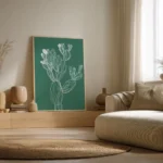Large framed white line art print of a prickly pear cactus on a deep green background, leaning on a wooden floor in a minimalist bedroom.