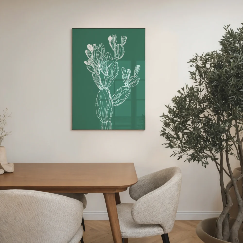 Framed white line art print of a cactus on a deep green background, displayed on a wall in a modern dining room with a wooden table and an olive tree.