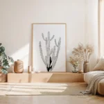 Black and white minimalist cactus art print with a light wooden frame, decorating a neutral-toned Japandi style bedroom with a low bed and natural light.