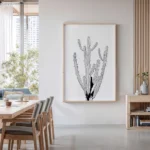 Black and white minimalist line art print of a tall cactus, displayed on a wall in a modern dining room with a wooden table and chairs.