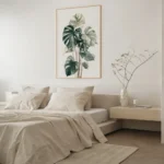 Framed art print of a Monstera plant, displayed on a light wall above a modern bedside table next to a bed with neutral-colored bedding in a bright bedroom.