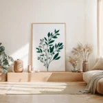 vertical framed art print featuring a dark green botanical sprig on a light background, leaning on a wooden platform against a neutral wall in a sunlit modern bedroom with a beige bed.