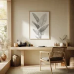 Black and white line art print of tropical foliage, displayed above a simple wooden desk and chair in a bright, minimalist home office space.