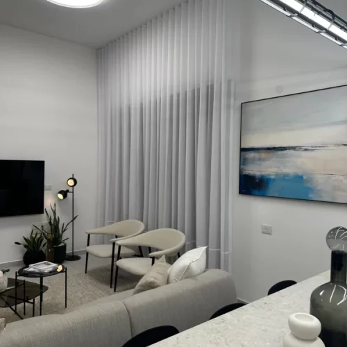 Modern living room with abstract art, TV, white curtains and minimalist decor.