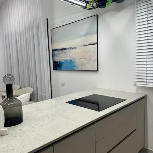 Modern kitchen with blue abstract wall art above white marble countertop.