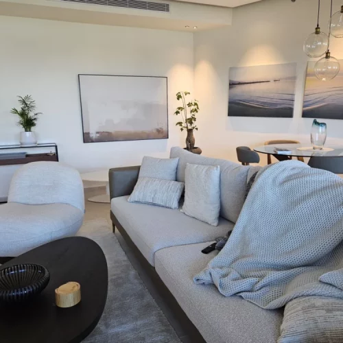Bright coastal living room with modern furniture and abstract seascape artwork.