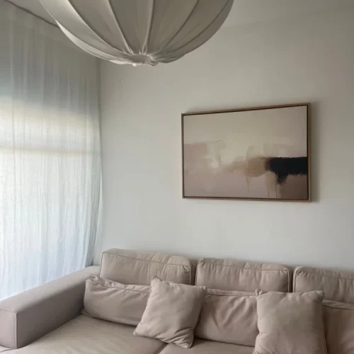 Minimalist living room with neutral sectional sofa and abstract wall art above.