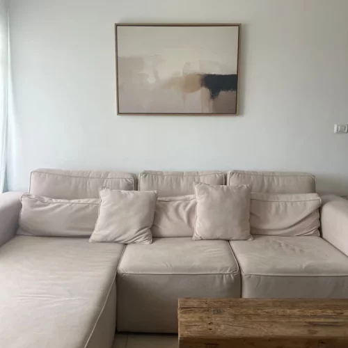Minimalist living room with beige sectional sofa and abstract art above rustic coffee table.